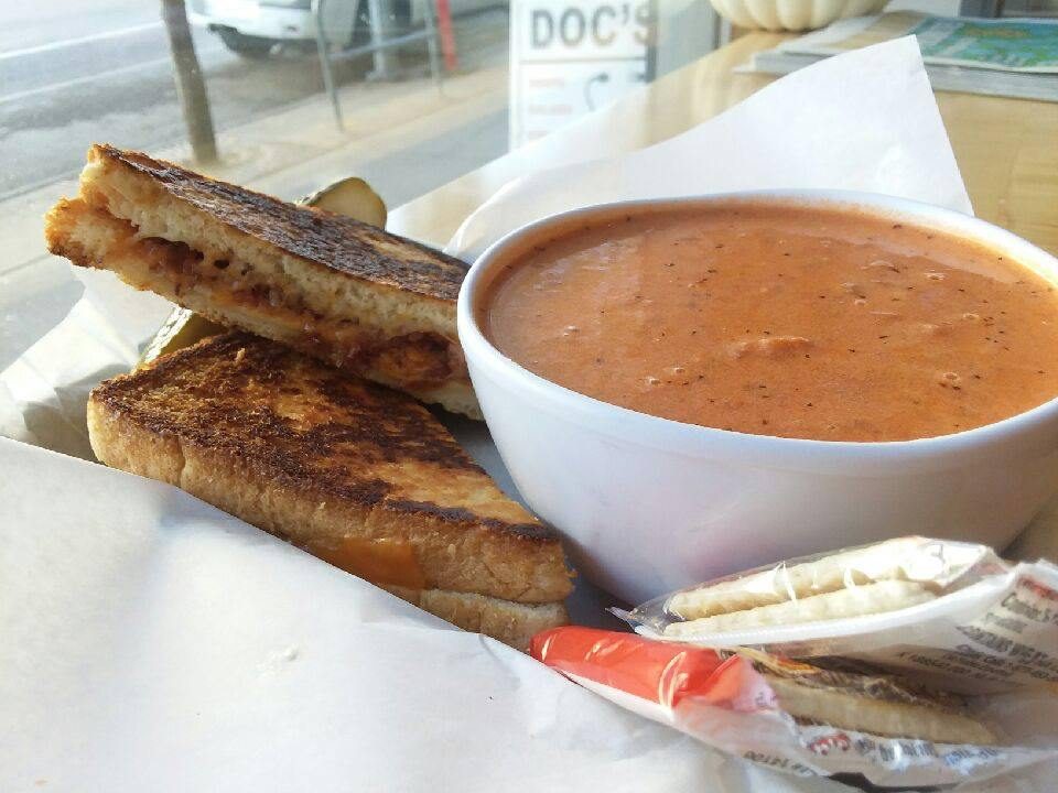 Bacon grilled cheese cut in half beside a bowl of tomato basil soup